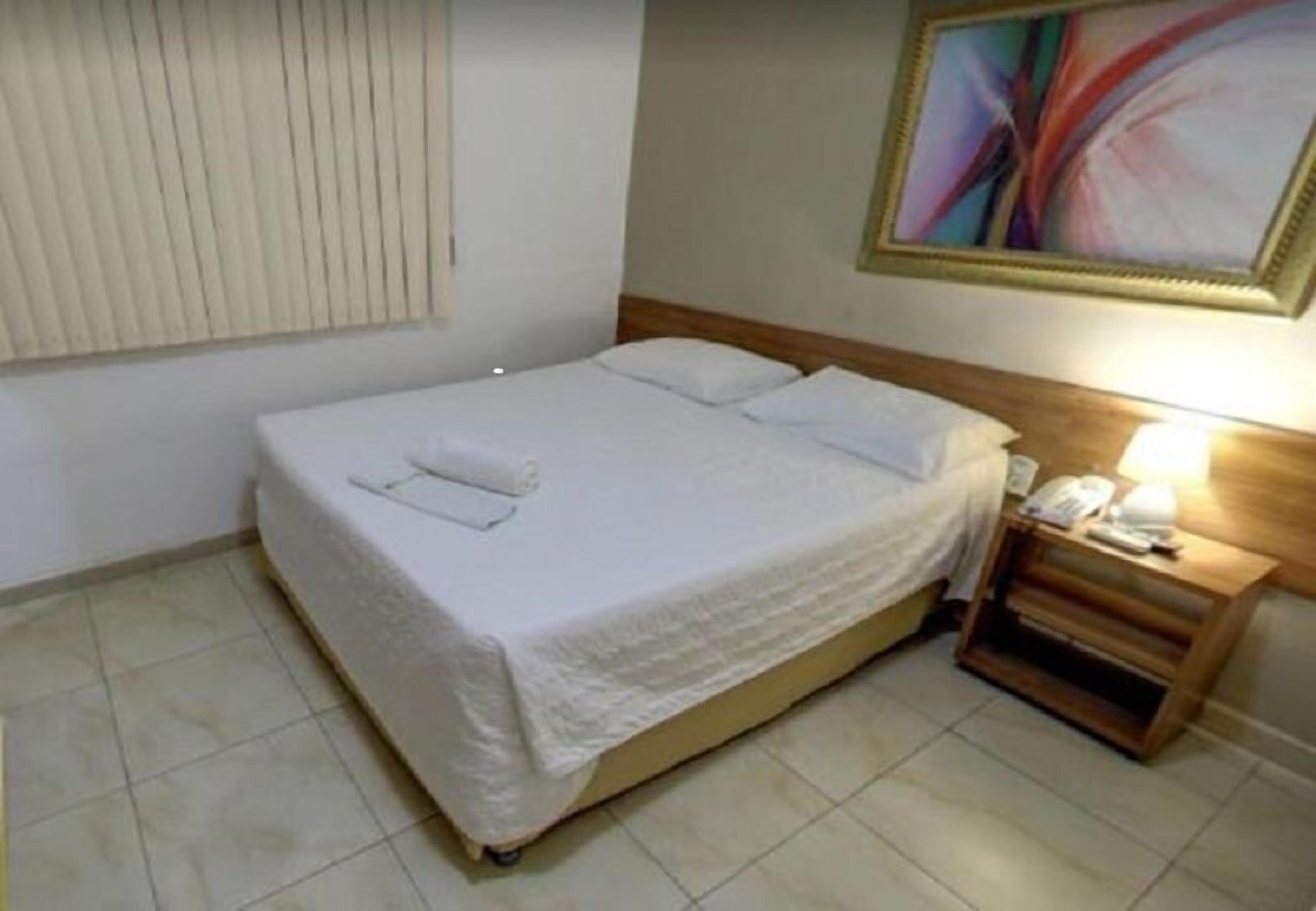 A neatly made bed with white linens and a wooden nightstand beside it.