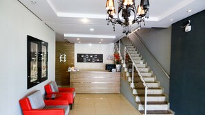 A hotel lobby with a reception desk, a staircase, red seating area, and a chandelier. - Ecos Conforto (Porto Velho)