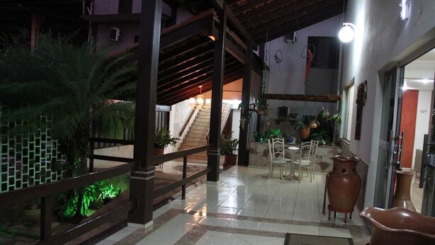 A hotel lobby with a tiled floor, a wooden staircase, and a seating area with chairs and tables.