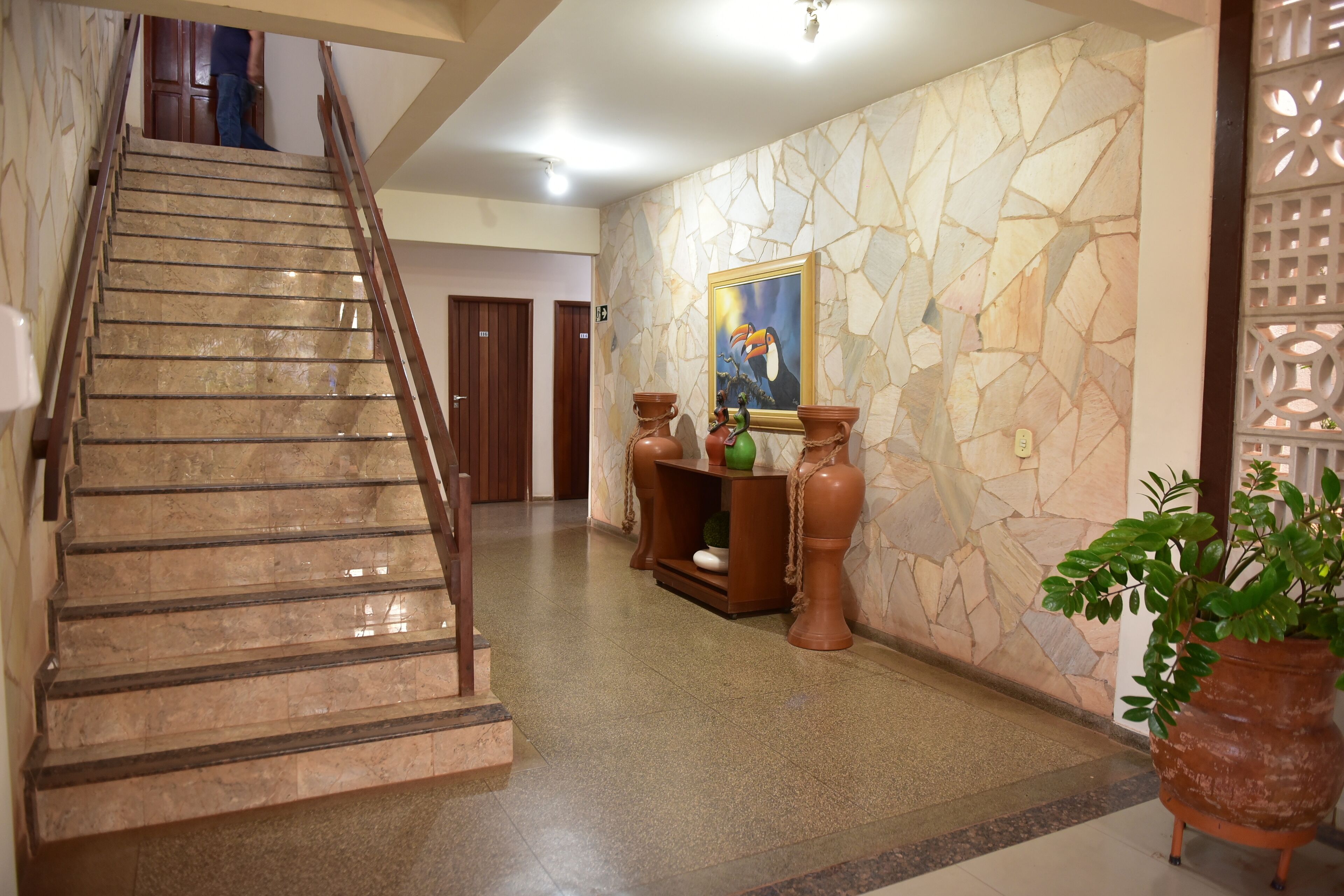 A marble staircase leading to a second floor, a stone wall with a framed painting, and a potted plant.