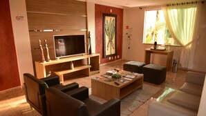 A modern living room with a flat-screen TV, wooden furniture, and a large window with curtains.