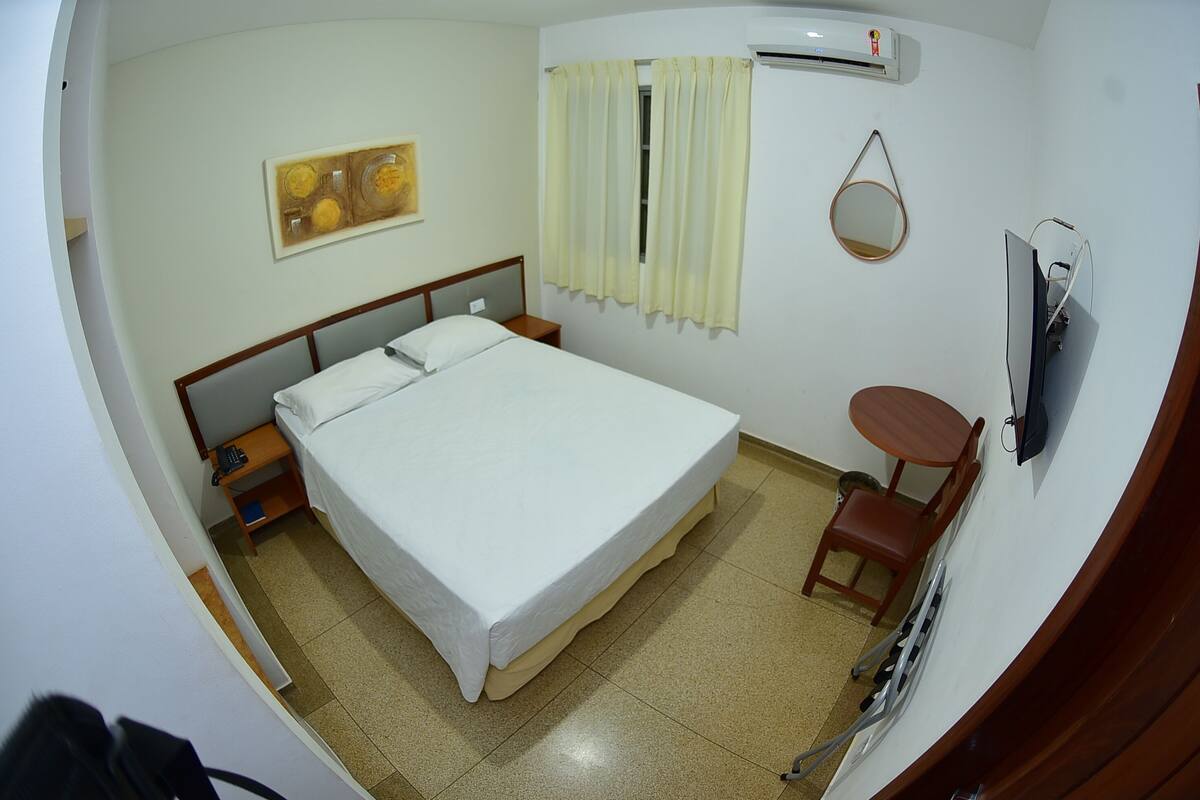 Habitació d'hotel amb llit, taula de nit, cadira, televisió i aire condicionat.