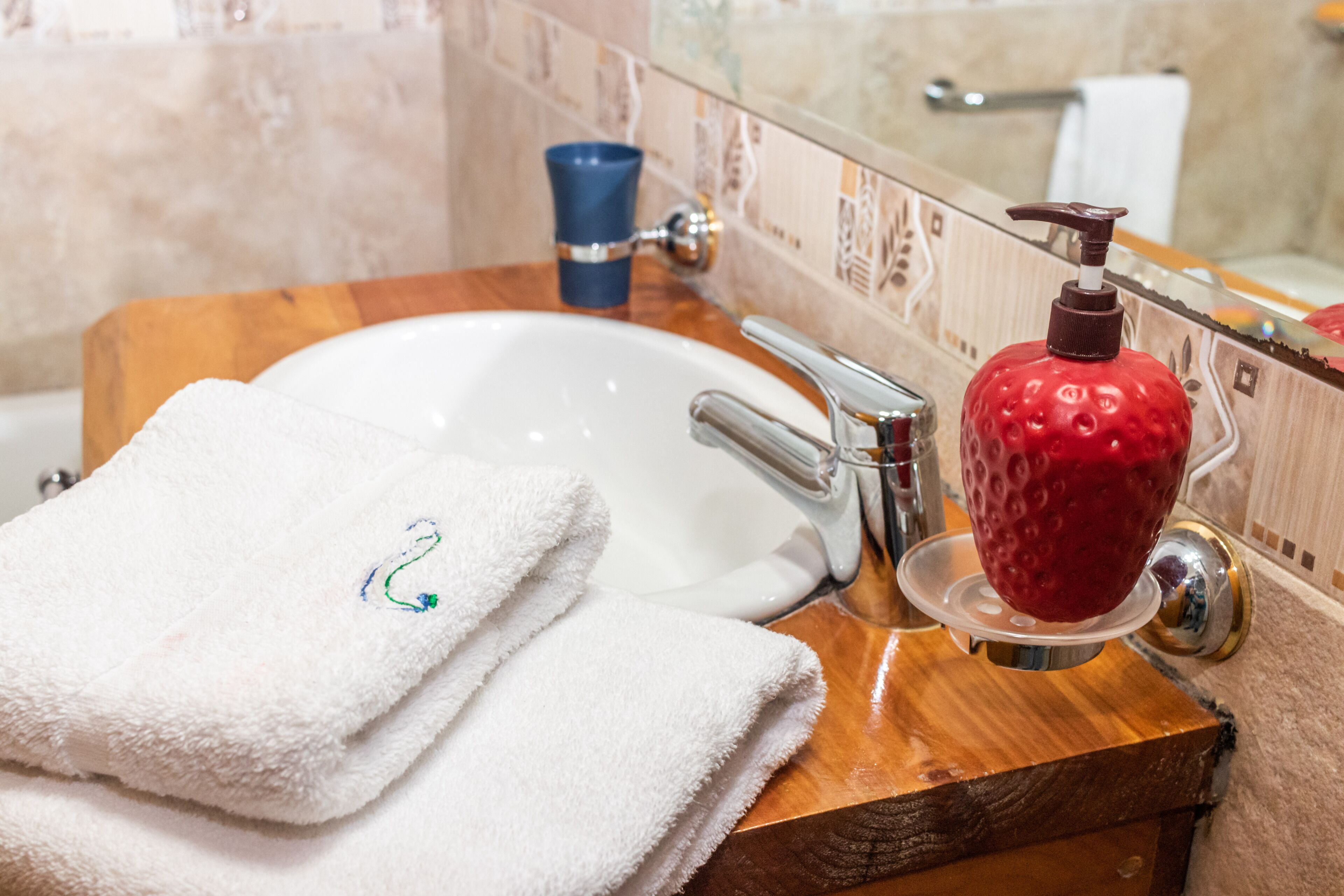 A bathroom with a wooden vanity, a white sink, a red soap dispenser, and a blue cup.