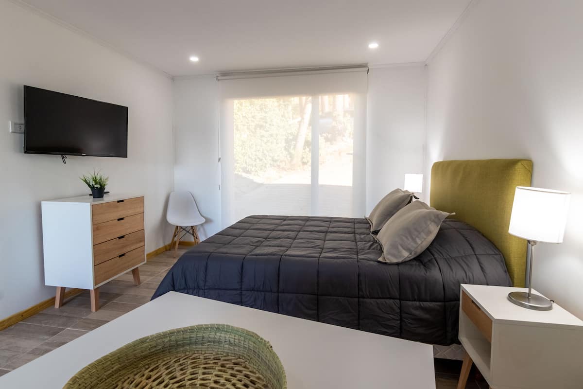 Quarto moderno com cama, televisão na parede, escrivaninha e cadeira.