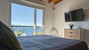 Une chambre avec un grand lit, un téléviseur fixé au mur et une vue sur la mer par une grande fenêtre.