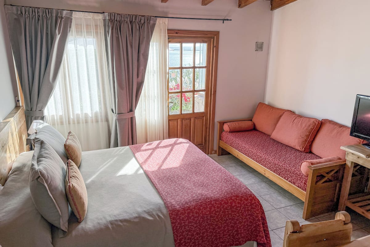 Quarto com cama, sofá, televisão e janela com cortinas.