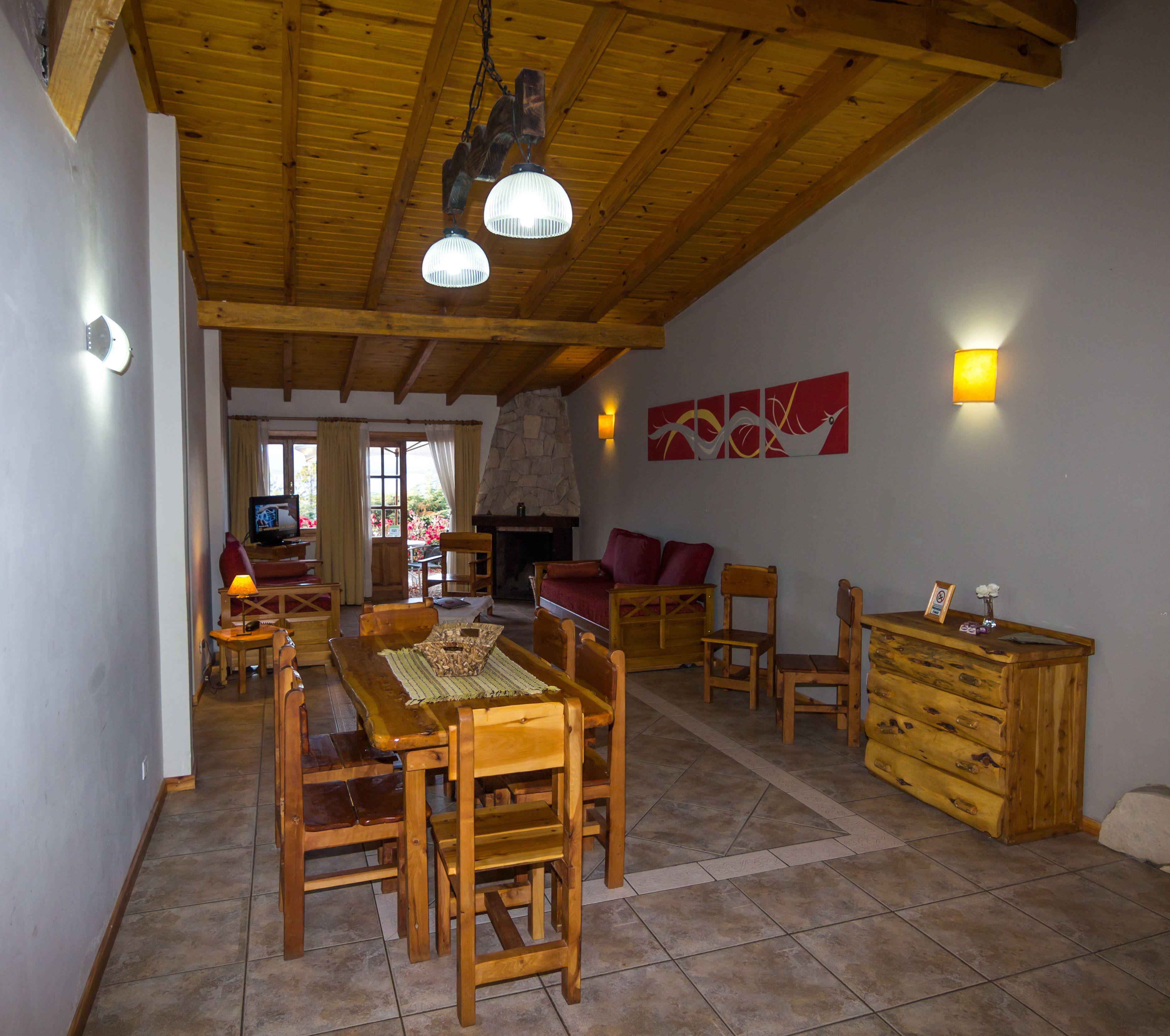 A spacious living area with a wooden dining table, chairs, a fireplace, and a stone wall.