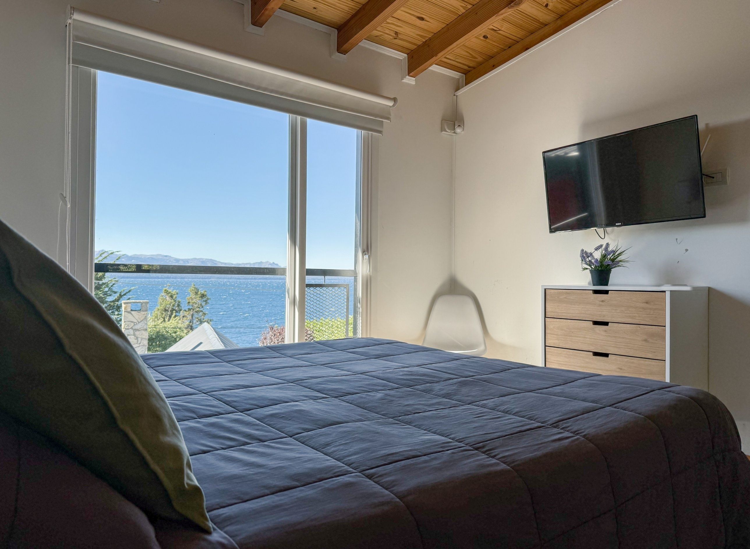 A bedroom with a bed, a TV, a dresser, and a window with a view of the sea.