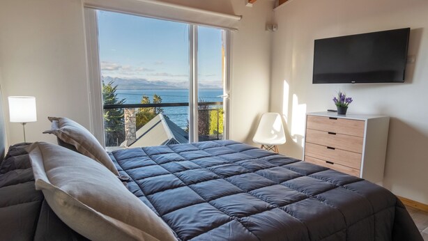 Une chambre dotée d’un grand lit, d’une télévision, d’une commode et d’un balcon offrant une vue sur la mer.