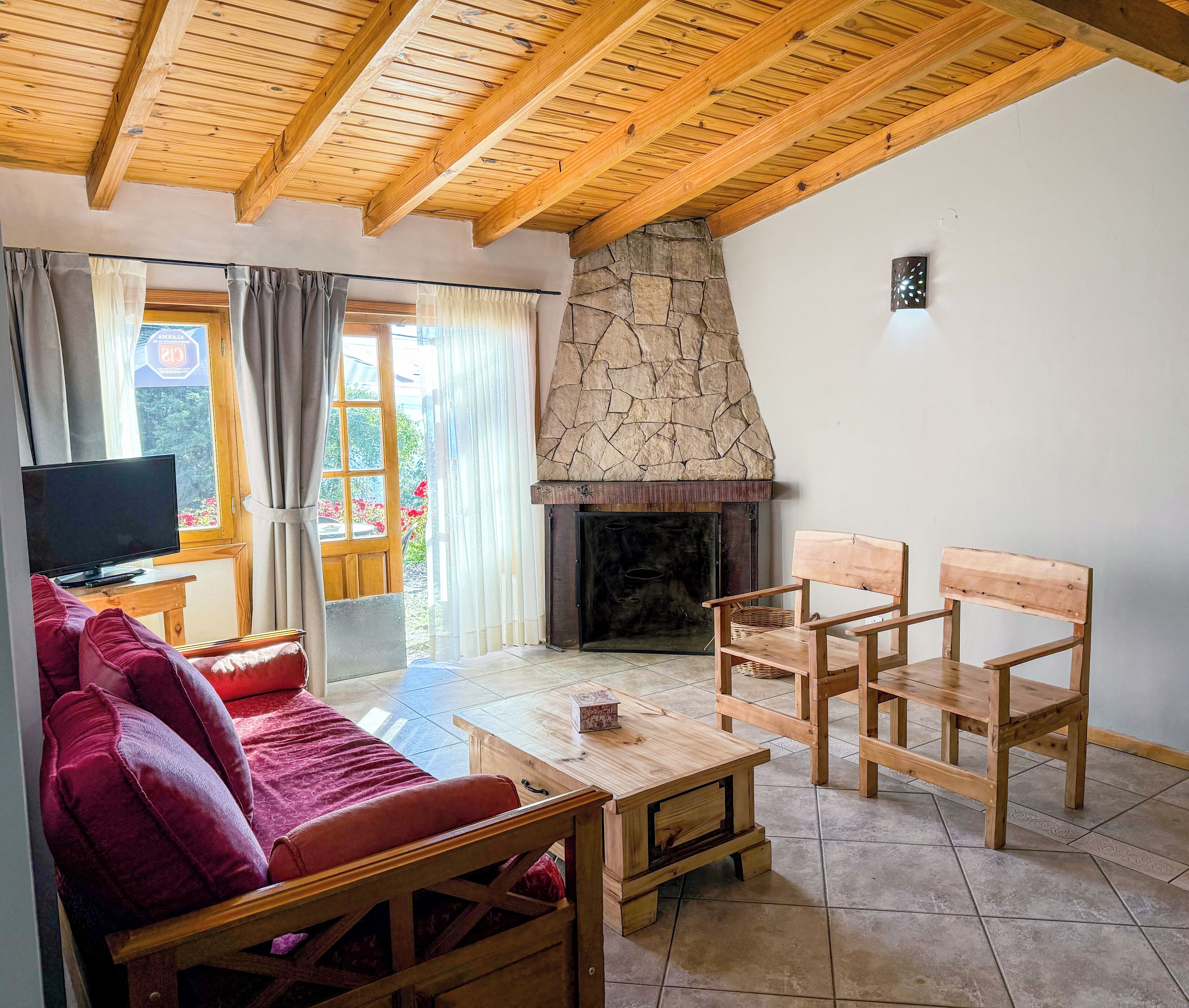 Ein gemütliches Wohnzimmer mit Kamin aus Stein, Holzmöbeln und einem Fernseher auf einem Schrank.