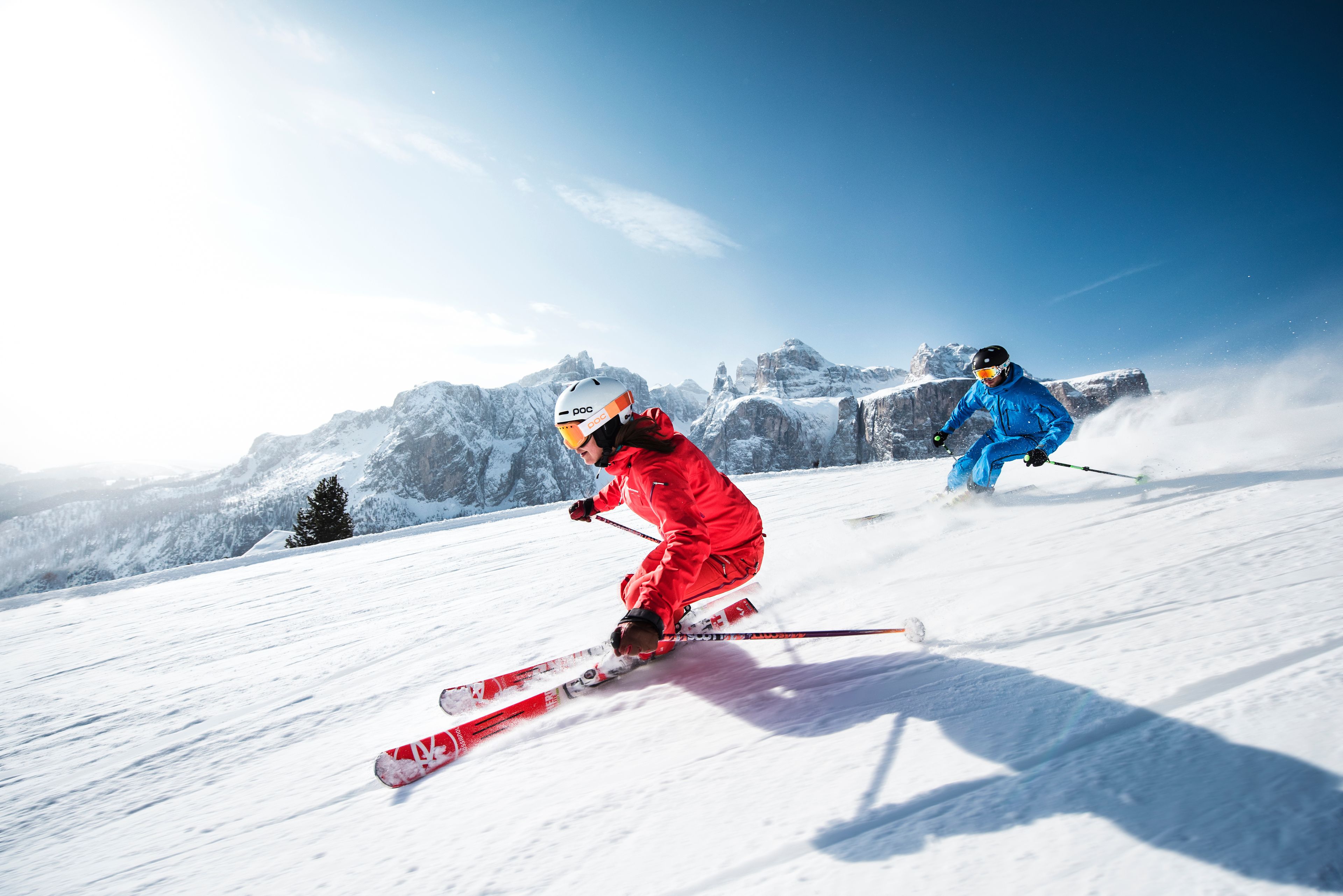 A person skiing down a snowy slope with a clear sky and mountains in the background.