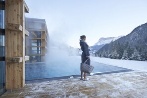 Una persona está de pie junto a un edificio de madera con vistas a montañas nevadas.