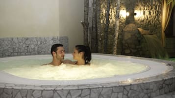 Ein Paar in einer Hottub-artige Steinwanne vor einer Steinwand mit Wasserspiel.