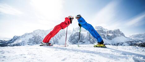 Two skiers in red and blue gear facing each other on a snowy mountain with a clear sky.