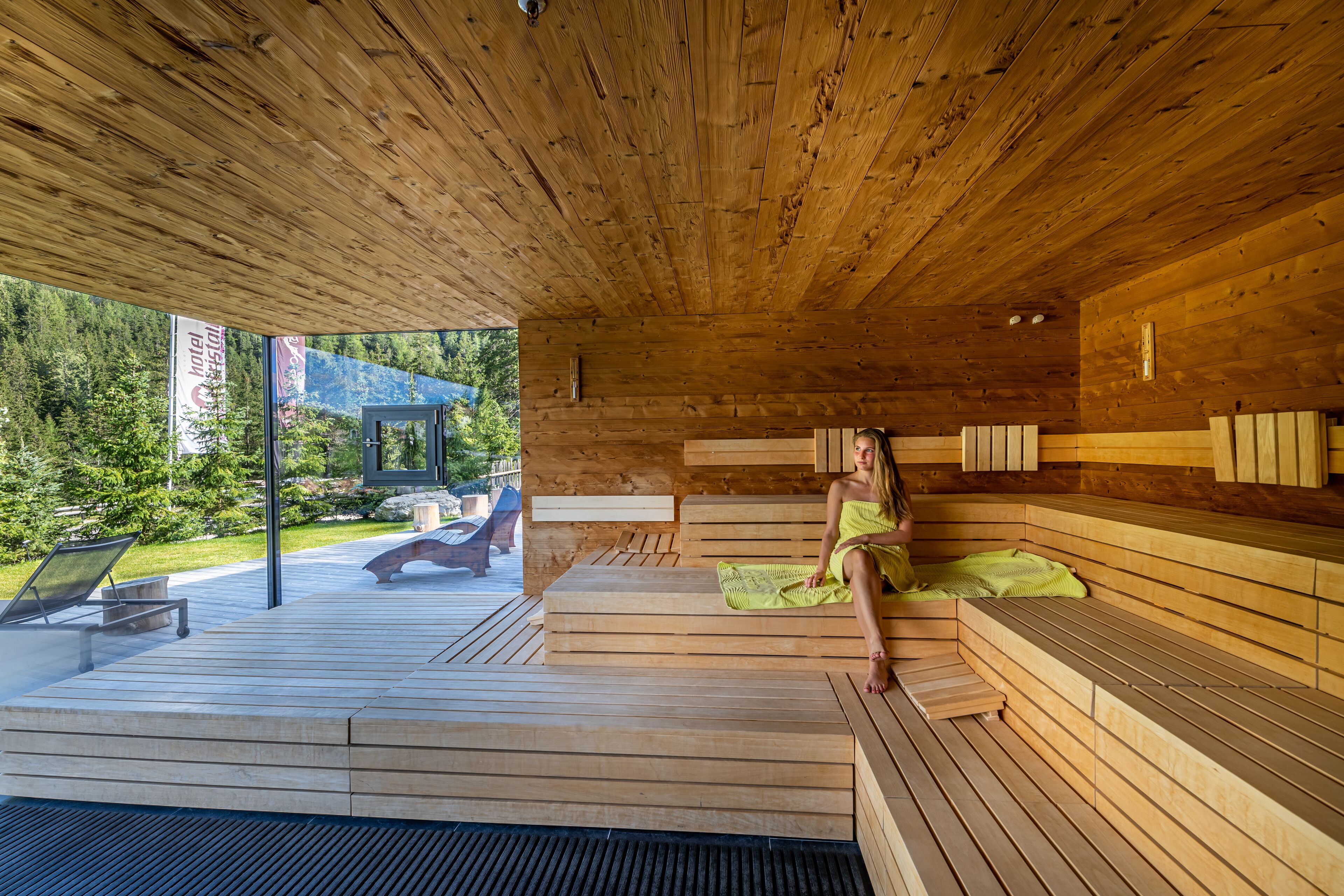 A wooden sauna with benches and a glass wall overlooking a garden.