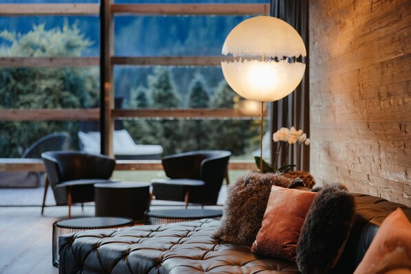 A modern living room with a leather sofa, round coffee table, and black chairs. A large, round, white pendant light hangs above the sofa. - Hotel Cristallo (Badia)