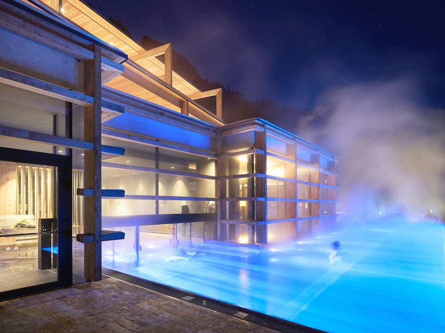 A modern building with a glass facade, a heated pool area, and a visible entrance.