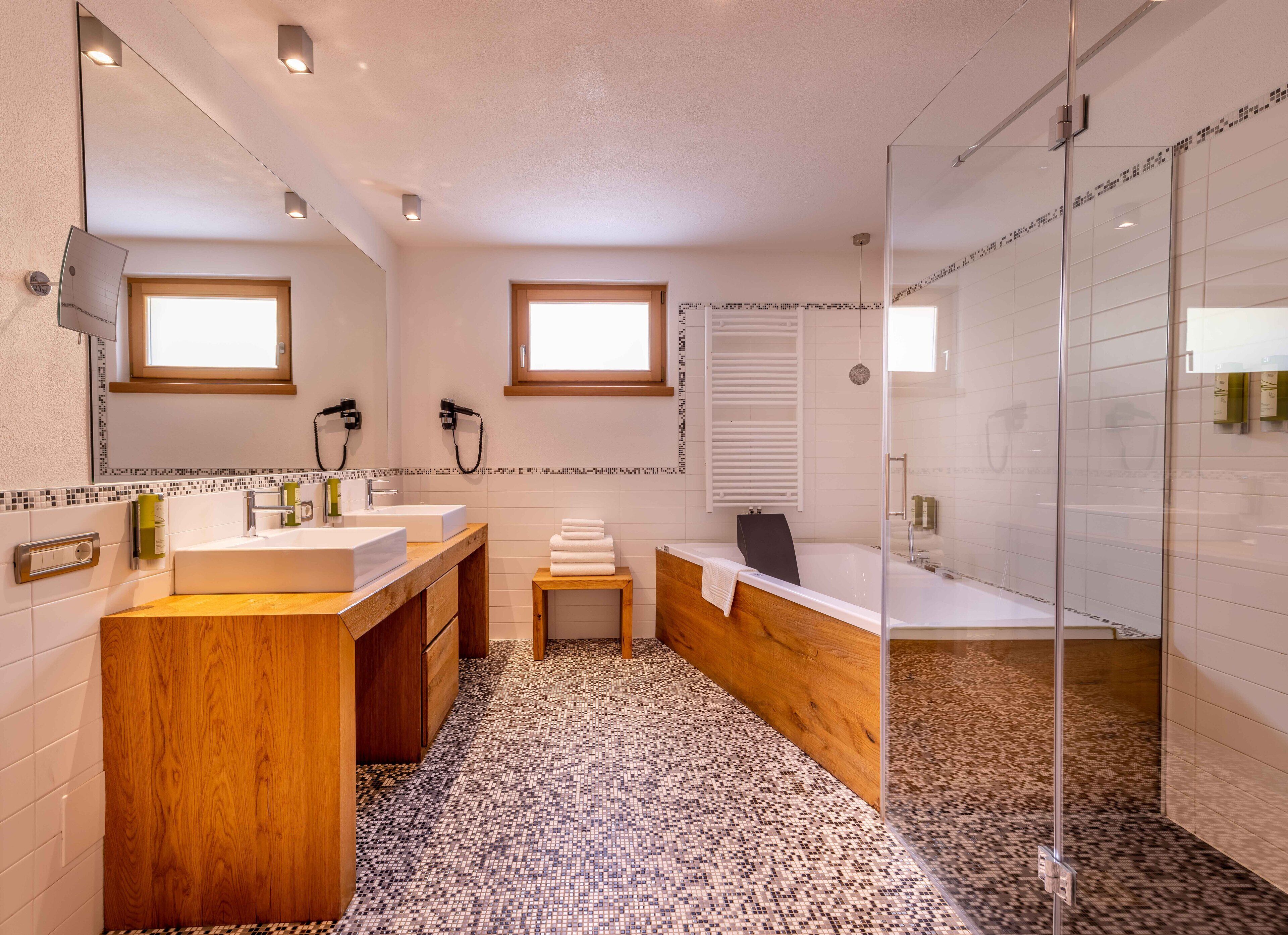 A modern bathroom with two sinks, a large mirror, a glass shower enclosure, and a small window.