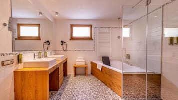 A modern bathroom with two sinks, a large mirror, a glass shower enclosure, and a small window.