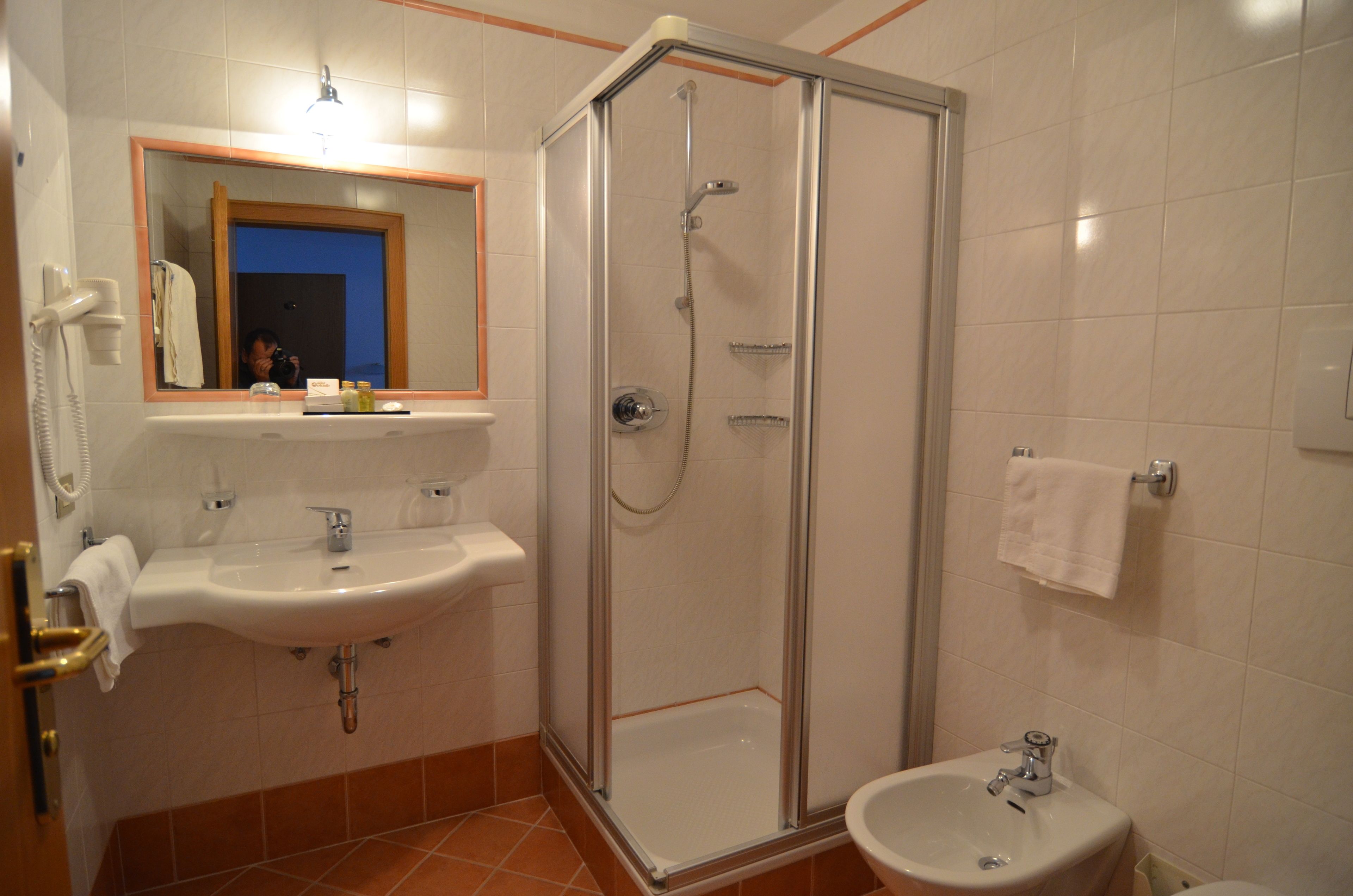 A bathroom with a shower, sink, and toilet, featuring a mirror, towel rack, and a glass-enclosed shower stall.