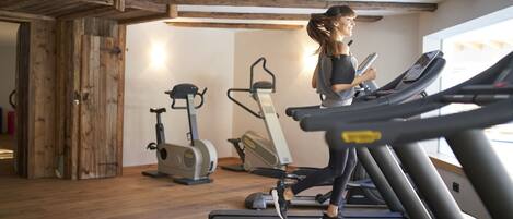Een fitnessruimte met loopbanden, hometrainers en een houten vloer.