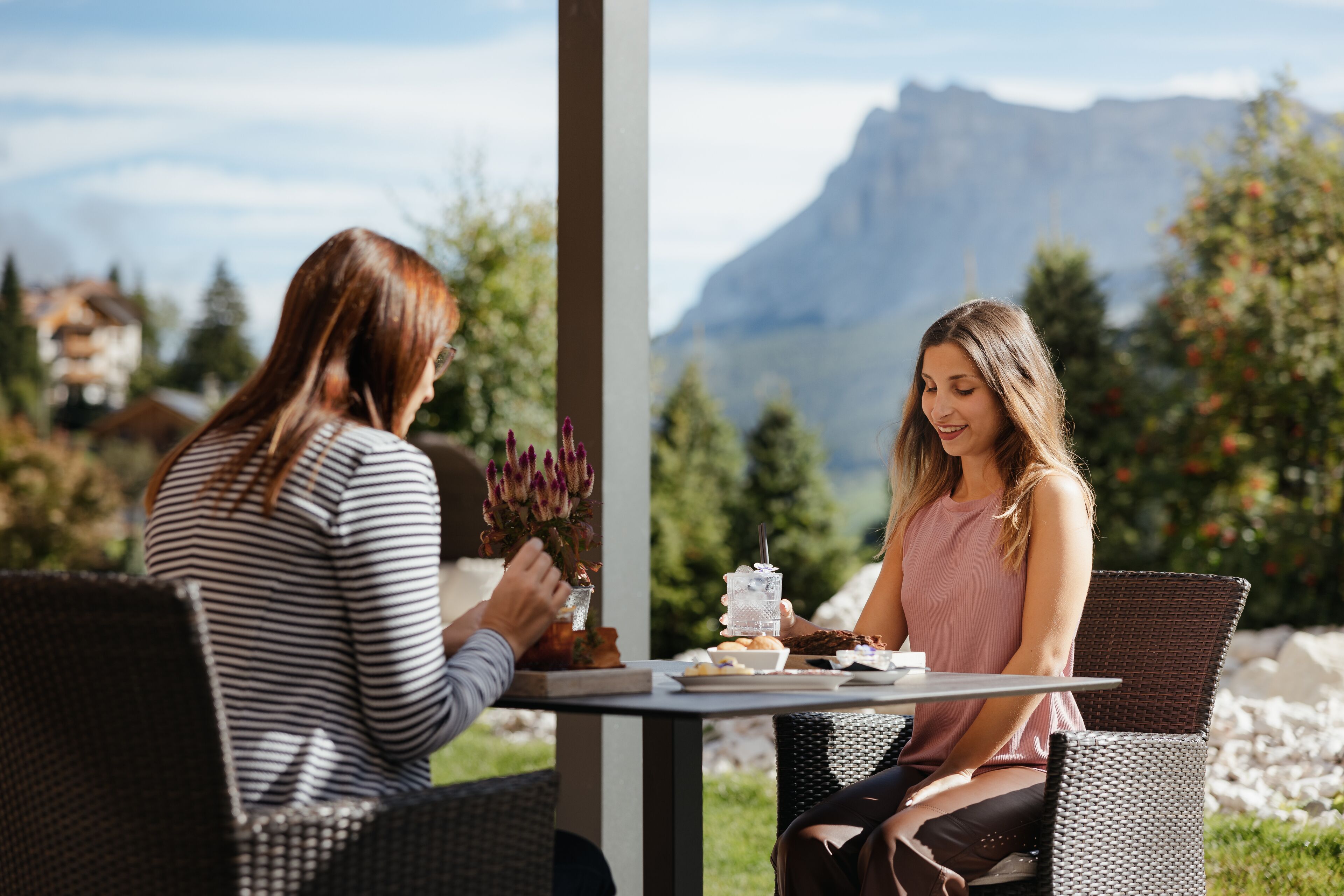 Två personer sitter vid ett bord utomhus med en bergskedja i bakgrunden.