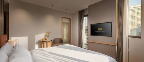 A hotel room with a bed, a TV mounted on the wall, a chair, and a small table with a vase of flowers.