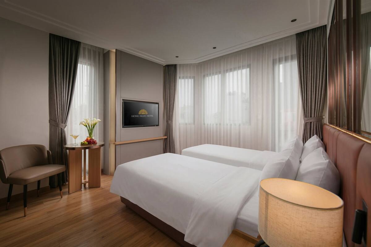 A hotel room with two beds, a TV, a desk with a lamp, and a chair.