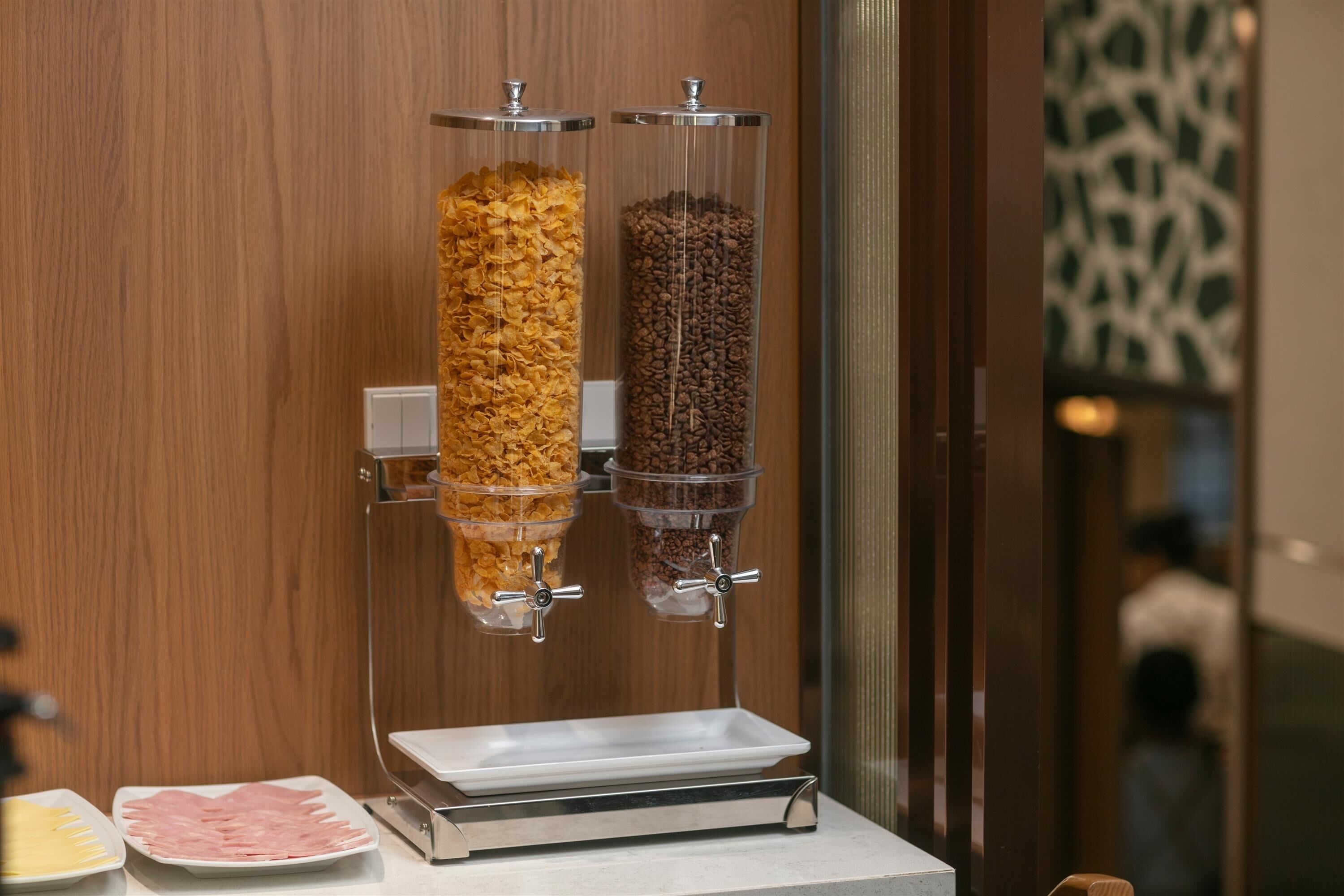 A buffet setup with two dispensers, one with orange-colored food and another with brown-colored food, and a white tray with plates of food.