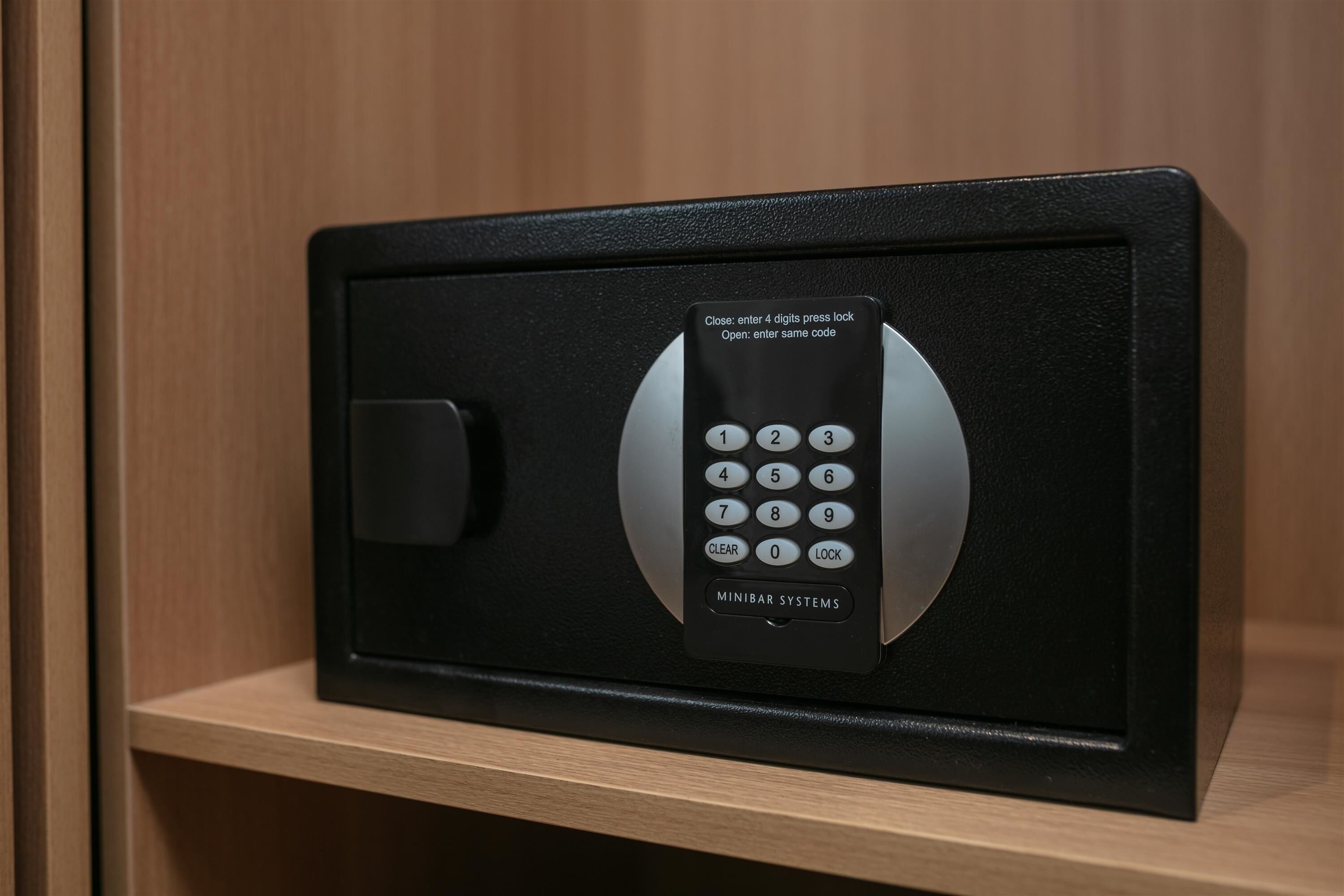 A black safe with a keypad, labeled 'MINIBAR SYSTEMS,' on a wooden shelf.