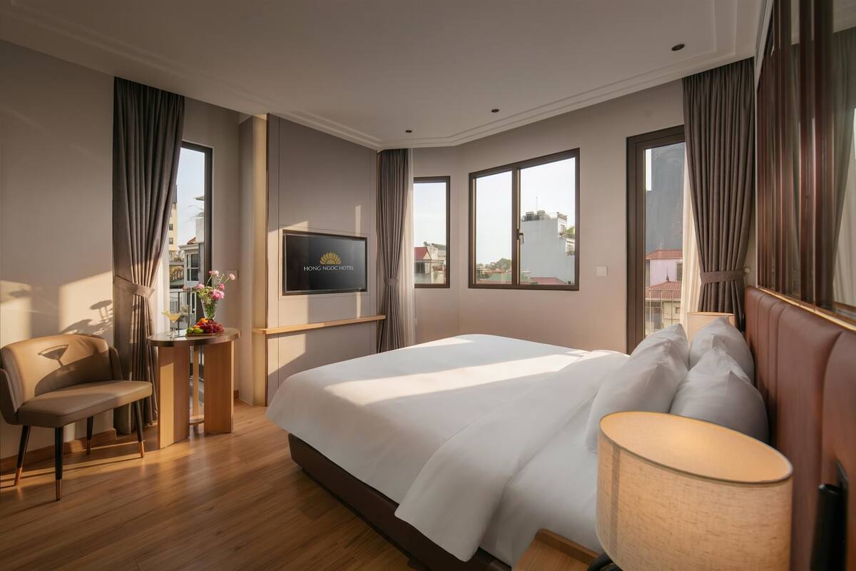 A hotel room with a bed, a desk with a TV, a chair, and a window with curtains.