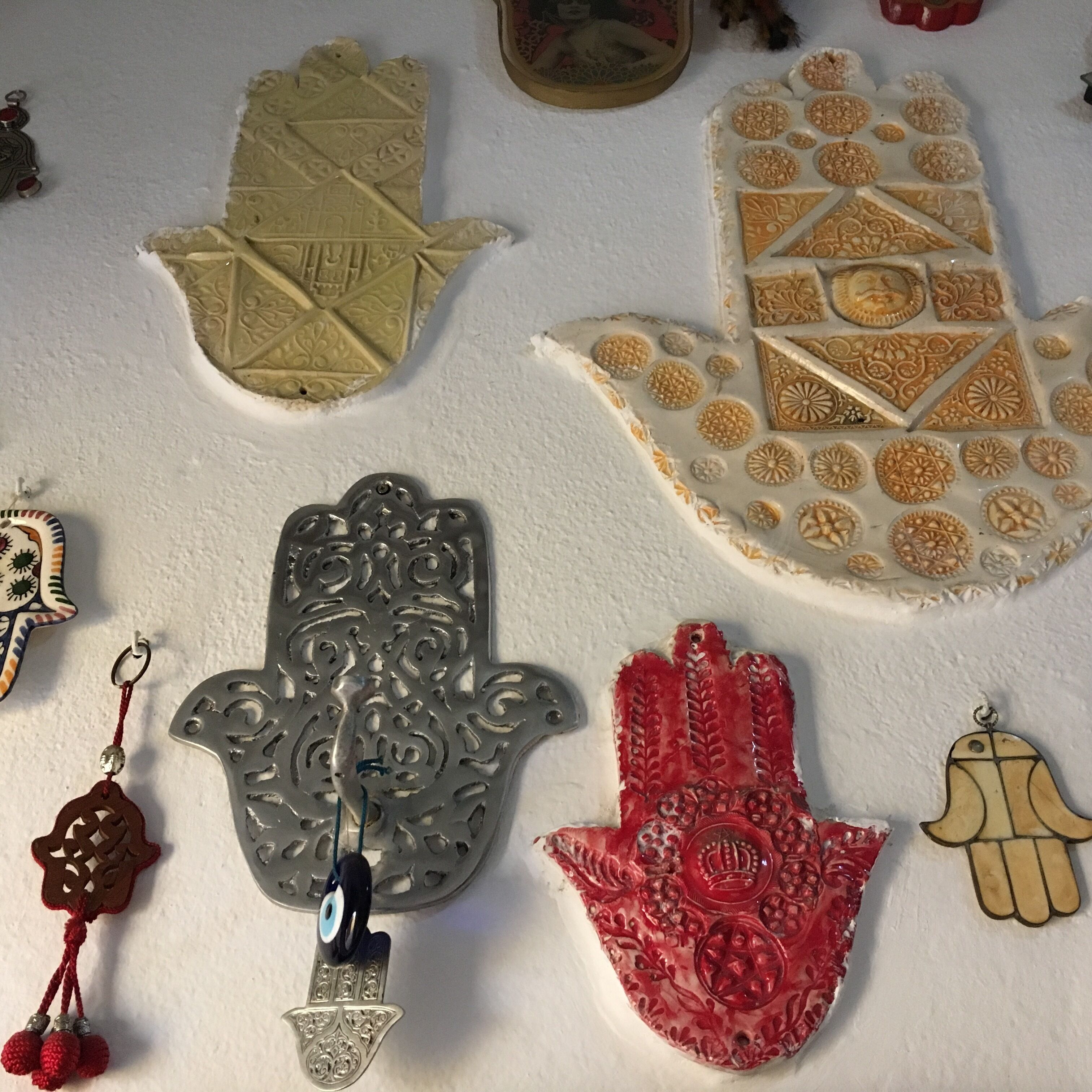Una colección de objetos decorativos, incluyendo un objeto con forma de mano con un ojo azul, un objeto con forma de mano rojo, y varios otros objetos con diseños variados.