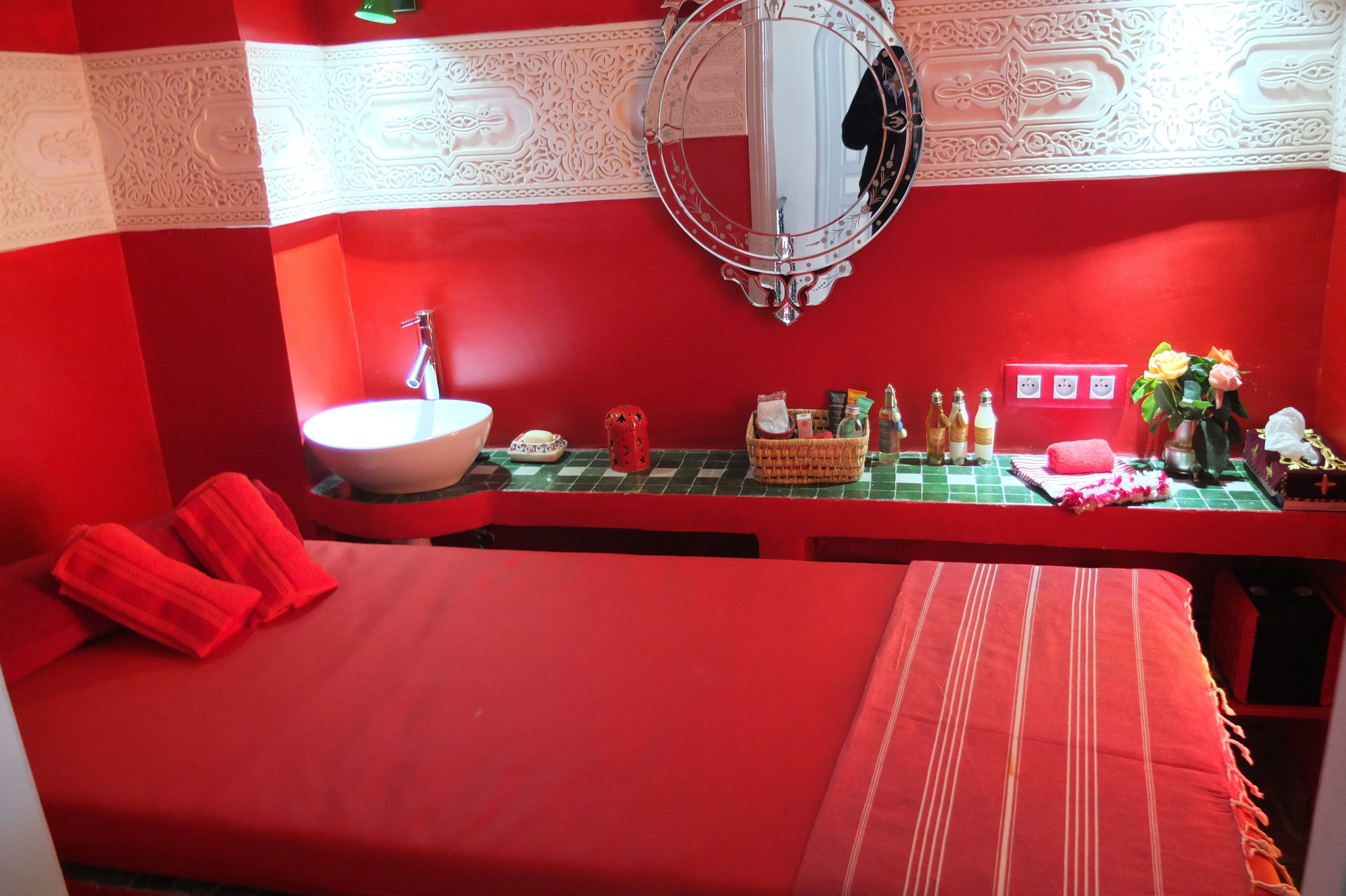 A red-themed room with a bed, a round mirror, a sink, and toiletries on the counter. - Dar Sultan (Tangier)