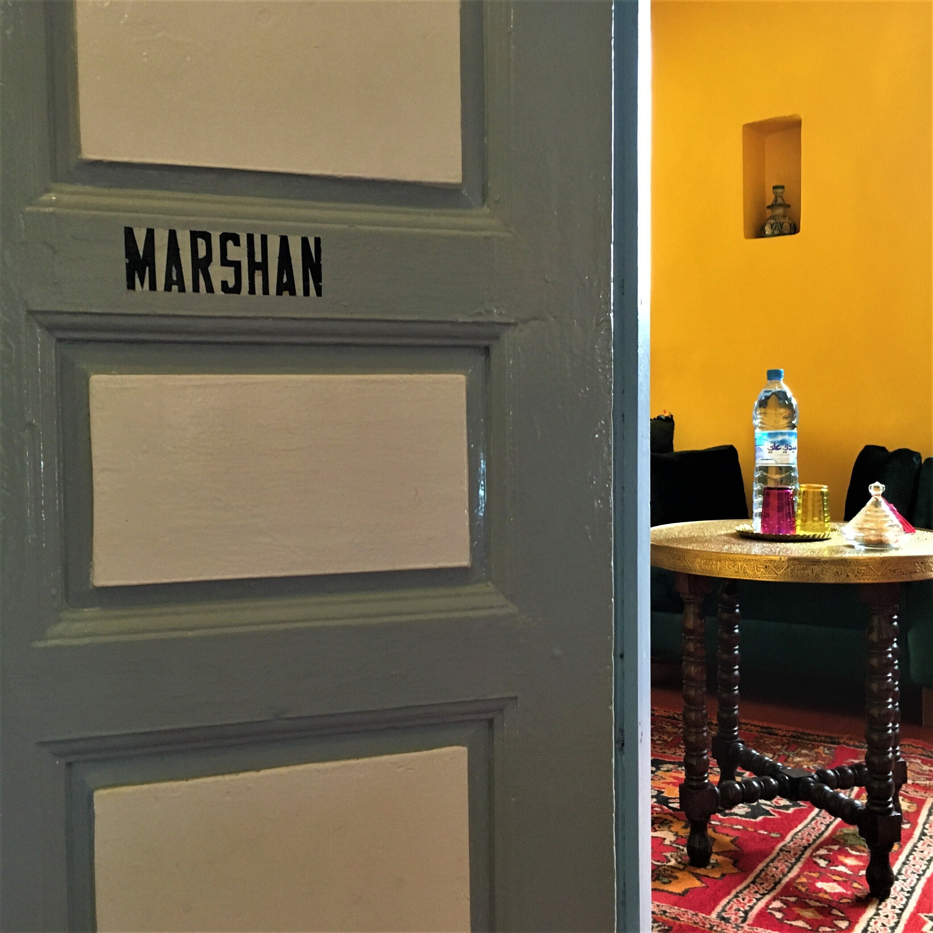 A room with a door labeled "MARSHAN" and a small table with a bottle and glasses.