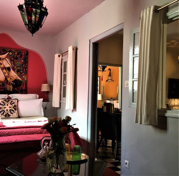 A bedroom with a bed, a nightstand, a vase with flowers, and a wall painting. - Dar Sultan (Tangier)