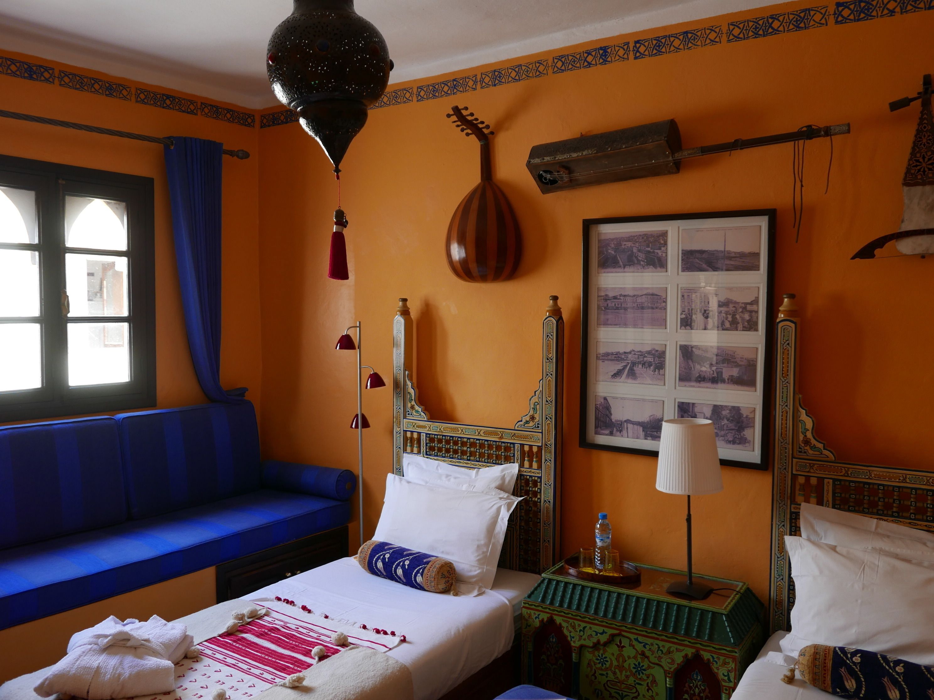 A room with a bed, a blue sofa, a hanging lamp, and a wall-mounted air conditioning unit.