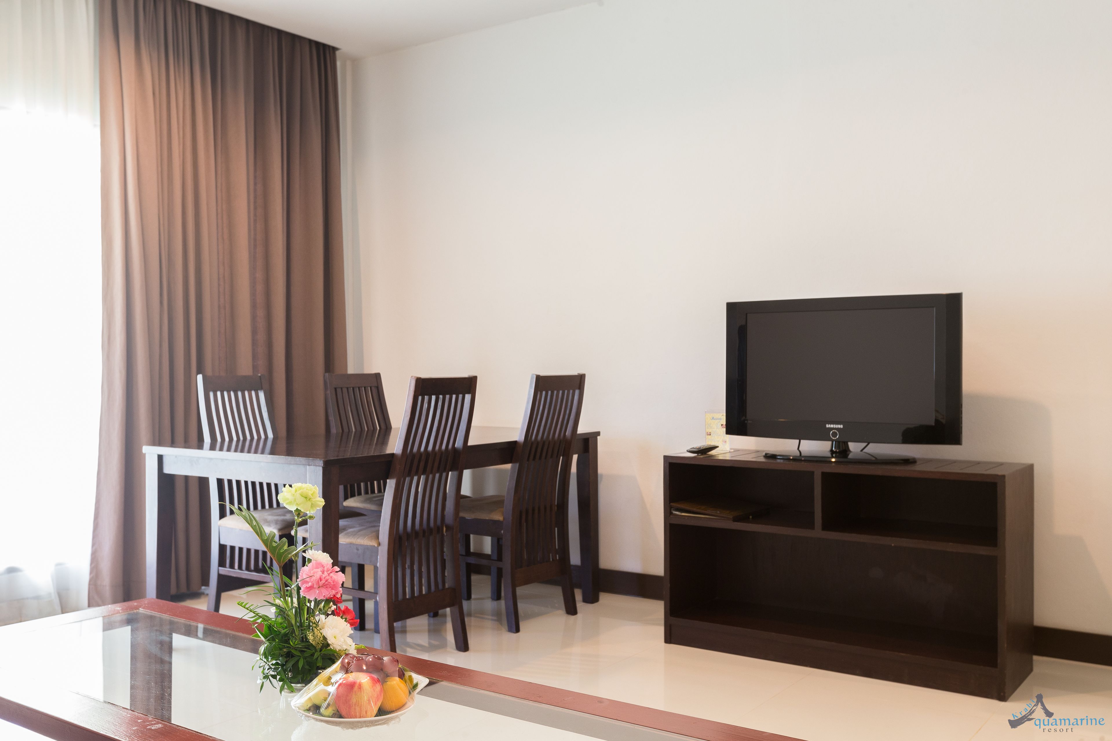 Una sala de estar moderna con televisor de pantalla plana, sillas de madera, una mesa de centro de vidrio con un centro de mesa floral y un mueble de entretenimiento oscuro.