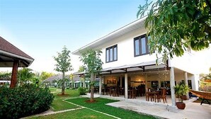 Une maison à deux étages dotée d’un patio couvert, d’une pelouse et de plantes en pot.