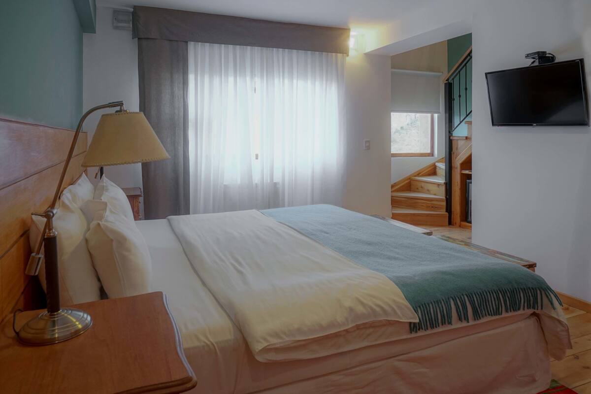 A hotel room with a bed, a bedside lamp, a TV mounted on the wall, and a staircase leading to another floor.