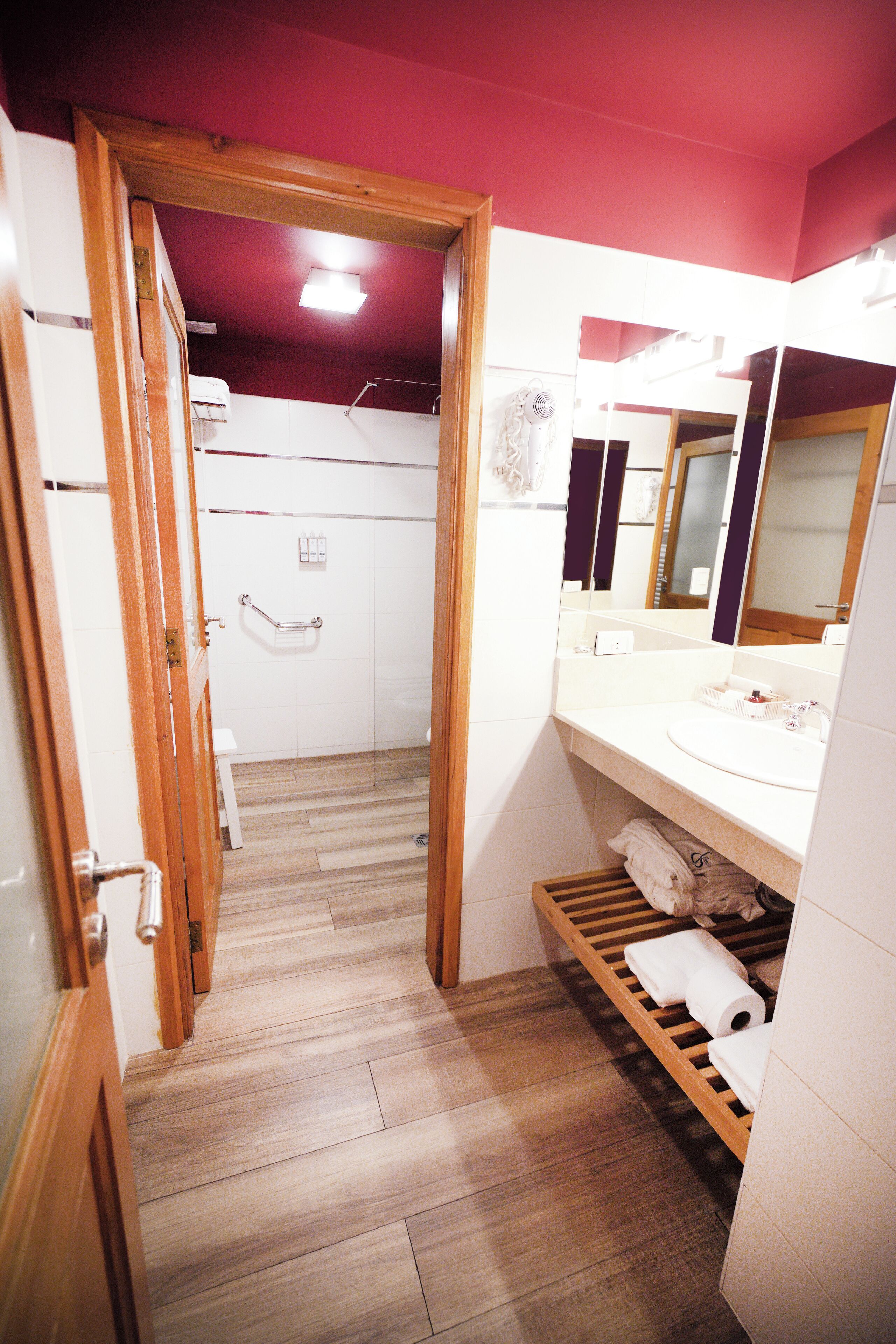A bathroom with a wooden floor, white tiles, a sink, a mirror, and a towel rack.