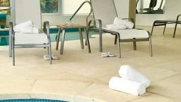 Relax by the pool surrounded by lush greenery and a glass wall offering a view of the outside.