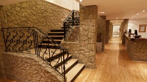 Uma escadaria com paredes de pedra e soalho de madeira, que conduz a uma área de receção com balcão e certificados emoldurados.