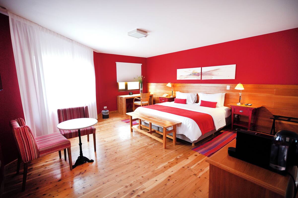 A hotel room with a bed, a desk, a chair, a table, and a TV.