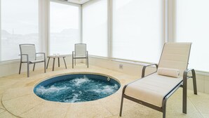 Uma piscina interior com hidromassagem, rodeada por cadeiras e uma mesa.