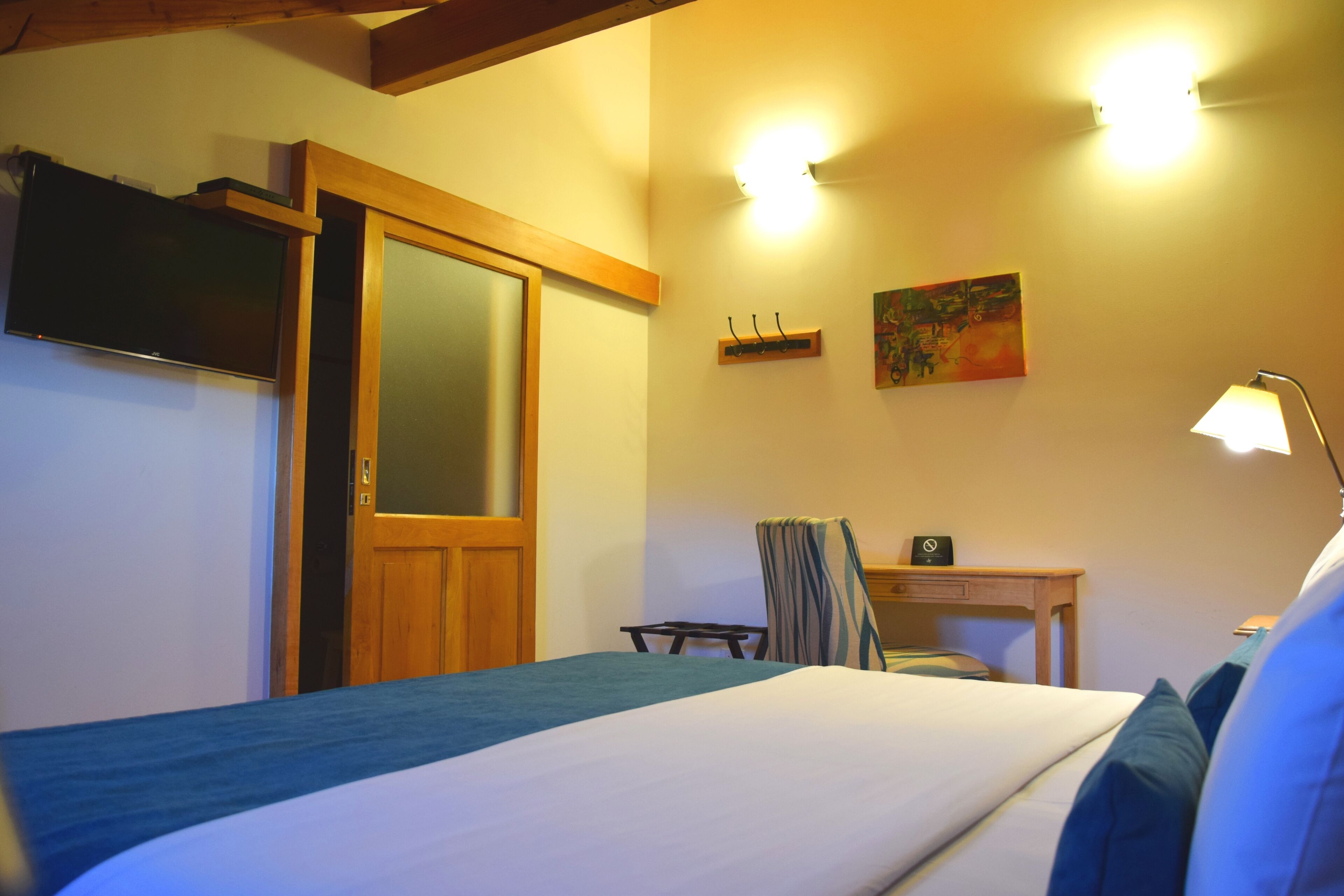 A hotel room with a bed, a desk, a chair, a TV, and a painting on the wall.
