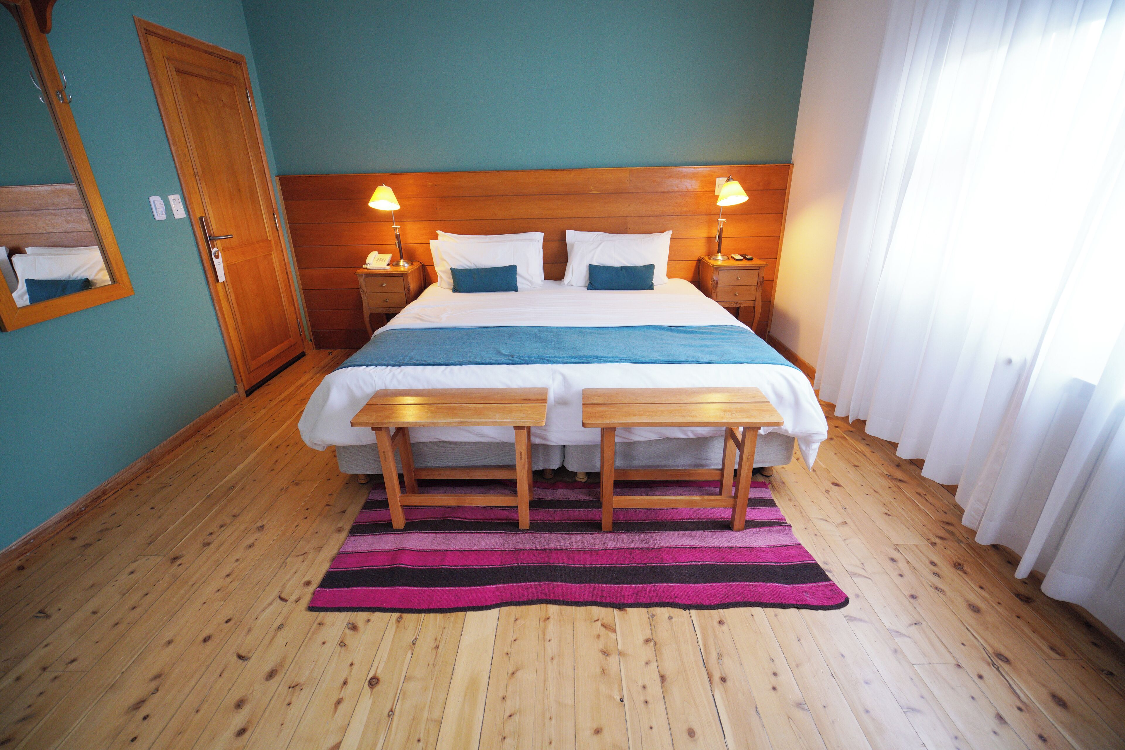 A neatly made bed with a wooden headboard, two bedside tables, and a striped rug on a wooden floor.