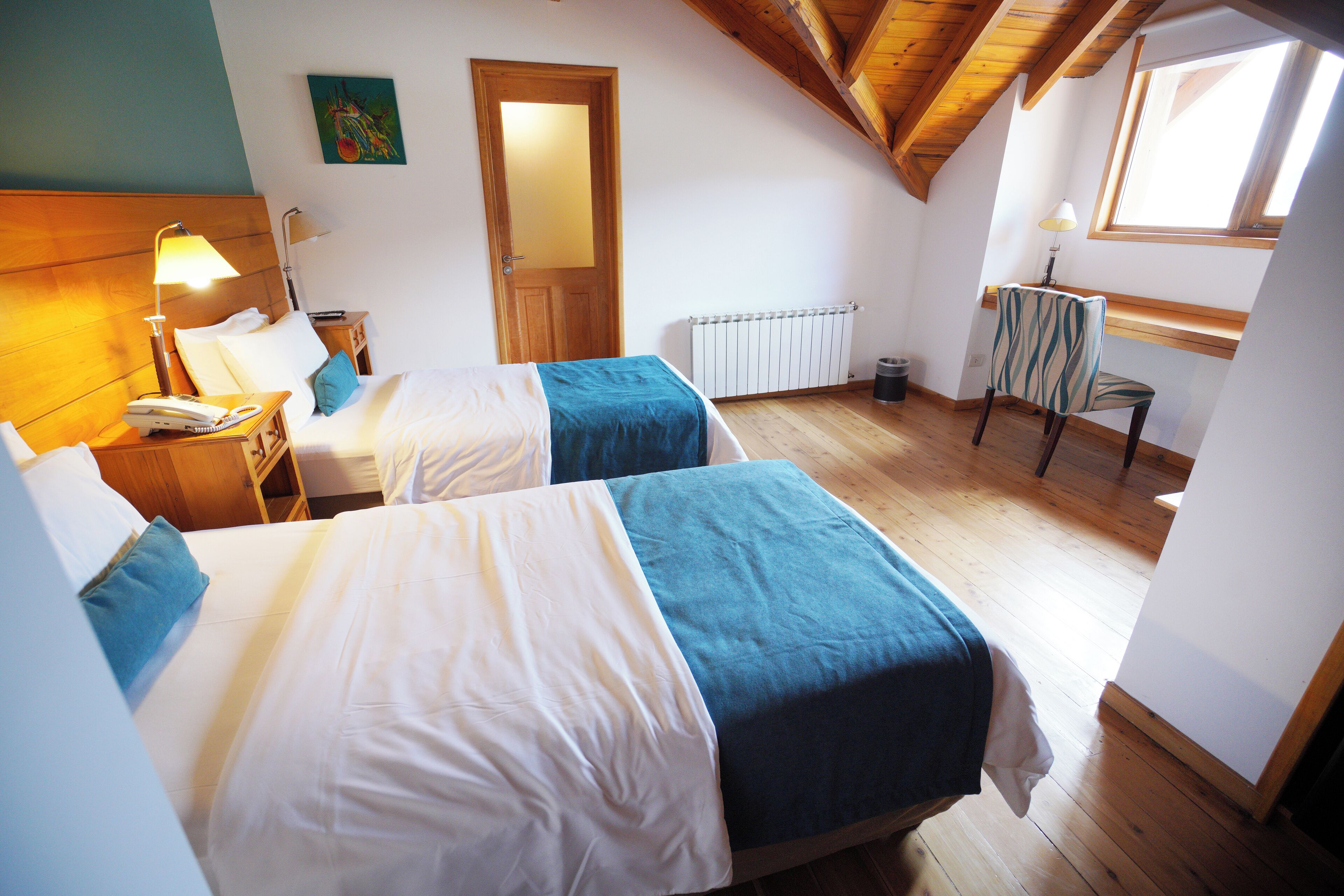 Ein Zimmer mit zwei Betten, Holzböden, einem Heizkörper, einem Schreibtisch mit Stuhl und einem Fenster.