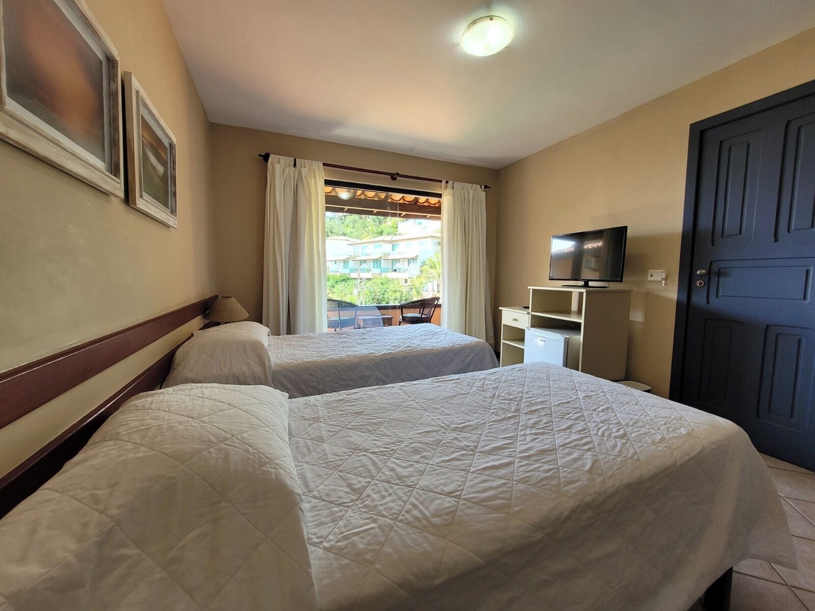 A hotel room with two beds, a television, a desk, and a door.