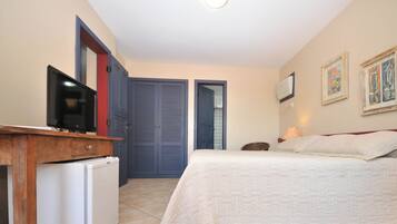 A bedroom with a bed, a television on a wooden desk, a wardrobe, and two framed pictures on the wall.