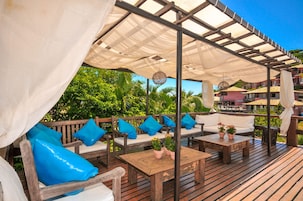 Eine Terrass mit Gartenmöbeln aus Holz, darunter Sofas und ein Tisch, unter einer weißen Markise.